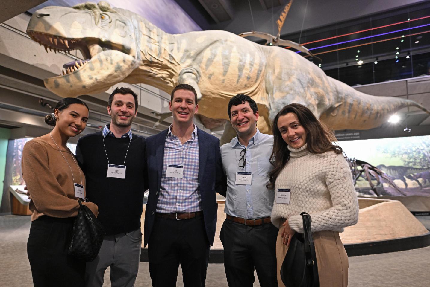 Alumni pose in front of a dinosaur exhibit at the 2023 Boston Holiday Party