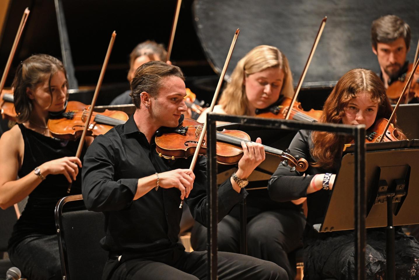 Students in the string section playing during a concert.