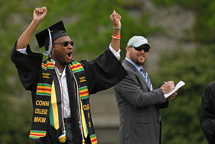 A graduate raises their arms and cheers as their name is called during commencement exercises