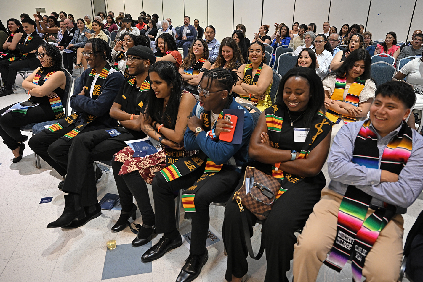 Seated students in stoles smile and cheer.