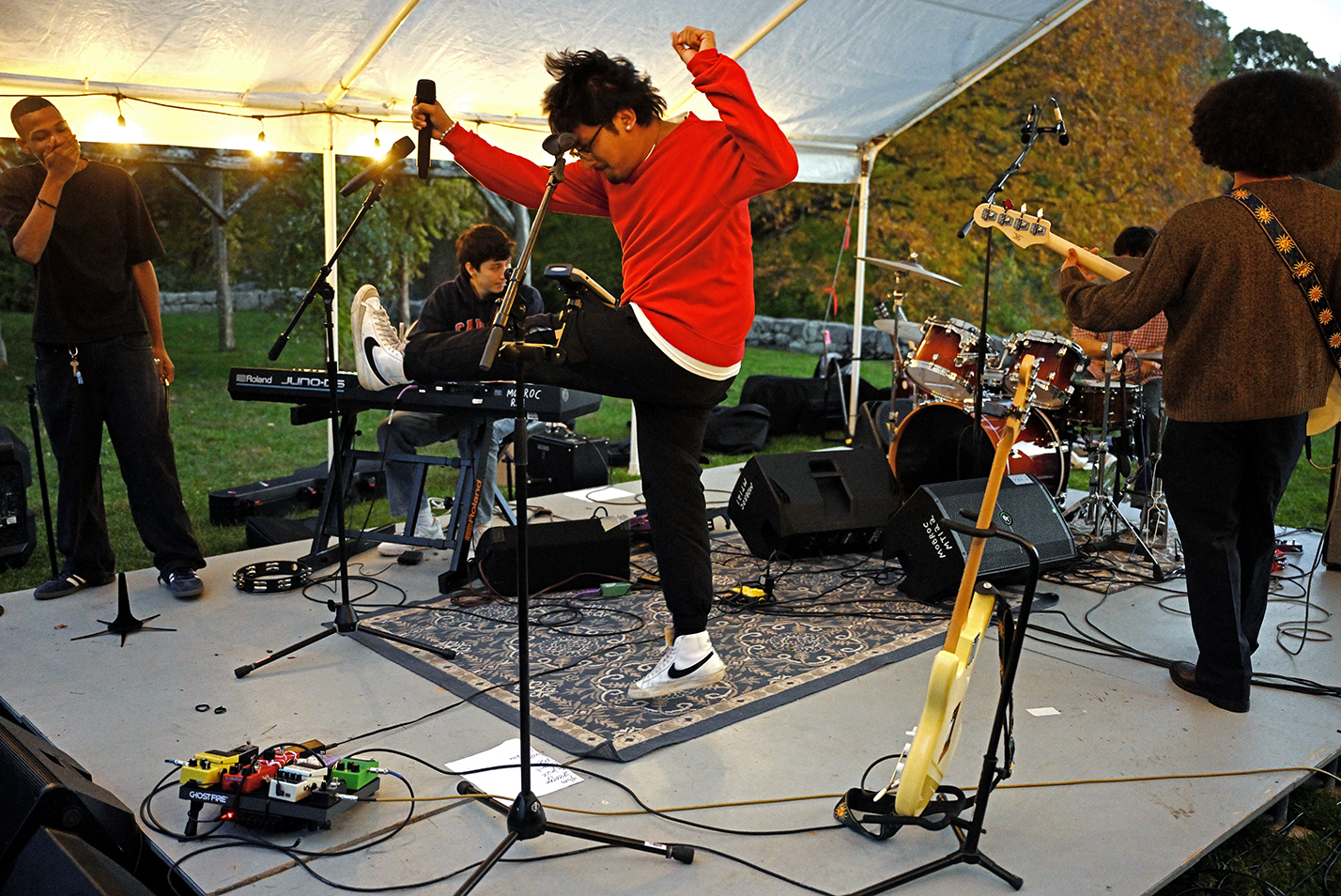 The lead singer in a rock band jumps in the air and kicks during an outdoor performance.