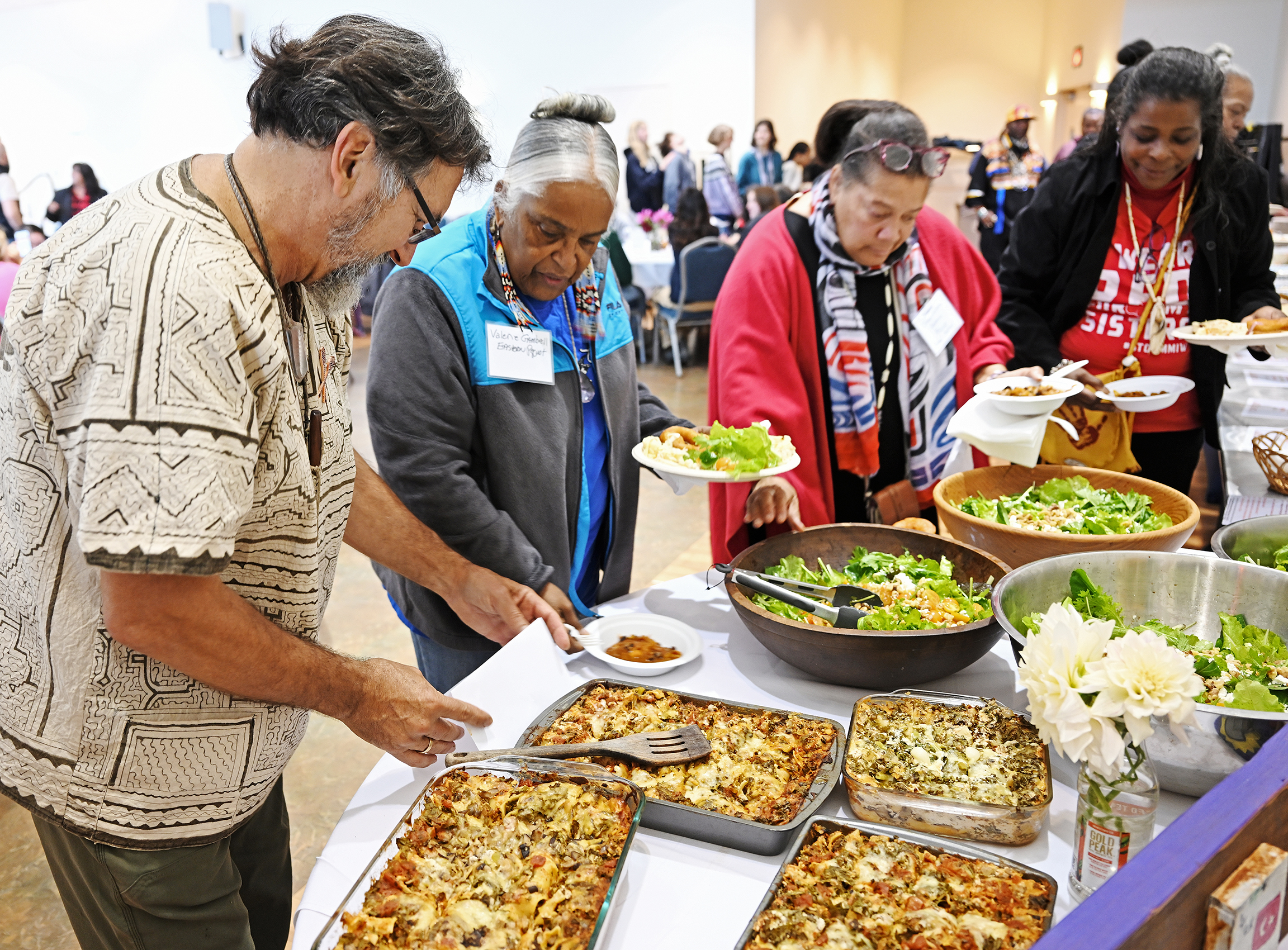 A man helps lunch guests to serve their food in a buffet line.