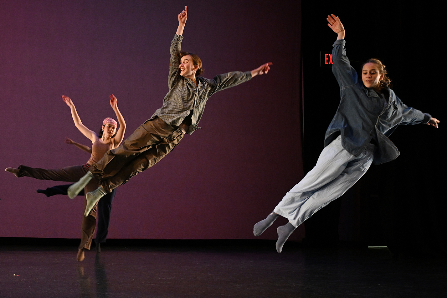 Three student dancers leap gracefully through the air performing a modern dance piece.