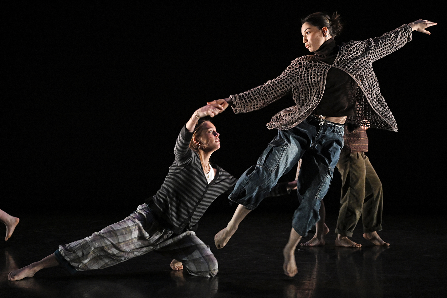 A dance student leaps gracefully in the air while performing a modern dance piece with other students.