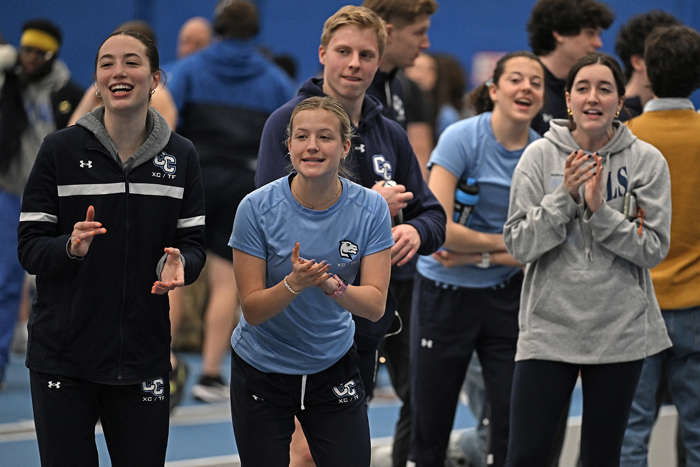 Track athletes cheer on teammates competing in a race at an indoor track meet.